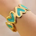 Golden heart-shaped C-style bangle with teal enamel inlay on a female wrist - Blue