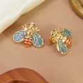 Detailed close-up of golden bee earrings with light blue enamel wings and red stripes - Dark Blue