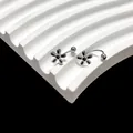 Detail van zilveren piercing sieraden met zwarte madeliefjes op een witte displaystand - Staal Bloem
