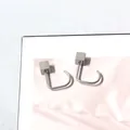 Detalle macro de pendientes geométricos de metal cepillado sobre seda de color rosa - Estilo Cuadrado con Gancho / Gris Plata