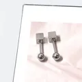 Detailopname van geometrische vierkante zilveren titanium oorbellen op roze satijn - Vierkante Draai Bal Stijl / Zilver