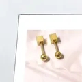 Detailopname van gouden geometrische oorbellen met kubus en bol op roze marmeren kaart - Vierkante Draai Bal Stijl / Goud