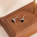 Gros plan sur des puces d'oreilles cœur argent et émail noir sur support en bois - Forme de Cœur