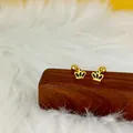 Détail de boucles d'oreilles couronne dorées avec émail noir sur support en bois - Couronne / Or