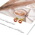 Detalle de pendientes de labios en esmalte rojo y oro sobre tarjeta decorativa - Labios Rojos