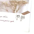 Detalle de pendientes de cruz plateados en tarjeta blanca decorativa con texto artístico - Plata Cruz