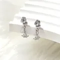 Close-up of silver titanium steel crown drop earrings on a white textured stand - Crown