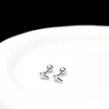 Primer plano detallado de pendientes de cruz plateados sobre un plato de cerámica blanca - Cruz