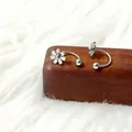 Detail van klaveroorbellen van titaniumstaal op een houten standaard en zachte pluche - Zilverkleurige Kleine Madeliefje U-Vorm Stijl