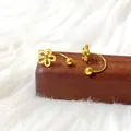 Detail van gouden titaniumstalen klaveroorbellen met U-vormig schroefontwerp voor vrouwen - Goudkleurige Holle Vijfbladige Bloem U-Vorm Stijl