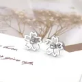 Detailopname van minimalistische madeliefje oorknopjes met parel op een geschenkkaart - Zilverkleurige Holle Vijfbladige Bloem Met Kraal Knopstijl