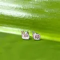 Vista macro de pendientes de caracol en metal pulido sobre un fondo de hoja verde - Caracol Bola de Rosca / Color acero