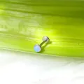 Dettaglio di un piercing labret in acciaio al titanio con opale blu su foglia verde - Pietra di luna