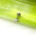 Dettaglio di un piercing argentato con lettera gotica K su una foglia verde fresca - Stile Lettera K Gotica