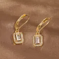 Close-up of golden rectangular drop earrings with zircon crystals on brown silk background - Gold