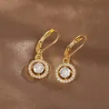 Detail of gold leverback earrings featuring a sparkling round crystal halo pendant - Gold