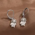 Detailed view of silver owl drop earrings with white zircon stones on velvet fabric - White Gold
