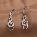 Macro view of silver treble clef earrings with cubic zirconia on brown satin - White Gold
