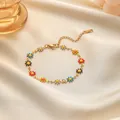 Bunte Emaille Gänseblümchen Armband aus goldenem Edelstahl auf beigem Seidenstoff - Armband / Bunte Gänseblümchen