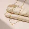 Minimalistische goldene Herz-Halskette auf beigem Leinenstoff mit warmem Sonnenlicht - Herzhalskette / Gold