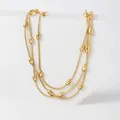 Detailed view of layered gold bead chain necklace displayed on white geometric stones - Gold Multi Layered Necklace (XKN6091)