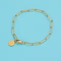 Dettaglio del bracciale a graffetta dorato con ciondolo rotondo lucido su fondo blu - 15cm / Oro