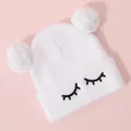 Detailed view of white knit hat featuring cute eyelash embroidery and dual faux fur pom-poms - One Size / White