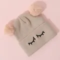 Dettaglio cappello bimbo in maglia con pompon rosa e ricamo a ciglia sul bordo risvoltato - Taglia unica / Beige