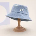 Light blue denim bucket hat with white ribbon bows on minimalist wooden display stand - 58cm Circumference / Light Blue