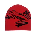 Detailed close-up of a red knit beanie featuring a large black abstract frog jacquard pattern - Red