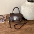 Detailed close-up of dark brown vintage saddle bag with silver metal lock on wood surface - With Charm / Brown