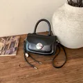 Detail of a vintage black saddle bag with silver buckle on a wooden desk with props - With Charm / Black