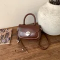 Detail of a brown vintage saddle bag with silver buckle and tassel on a wooden desk - With Charm / Brown