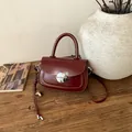Detail of burgundy vintage saddle bag featuring a large silver buckle on dark wood surface - With Charm / Burgundy