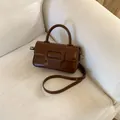 Detail of a brown leather crossbody bag with a square buckle on a beige sofa - Brown No Pendant