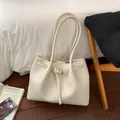 Detail shot of beige lychee grain leather tote bag featuring a metallic buckle strap - White