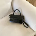 Detail of minimalist black glossy leather handbag with large buckle on a white sofa - Black without Pendant