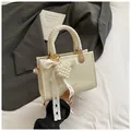 Detail van crème crossbodytas met geweven handvat en parelmoeren hartjeshanger - Broken Wit