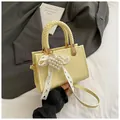 Detail van lichtgele crossbodytas met geweven handvat, parelhart hanger en kanten lint - Geel