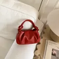 Detail of red pleated cloud bag featuring a knotted handle on a soft white sofa - Red