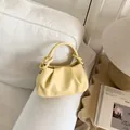 Detail of soft yellow pleated dumpling bag on a stylish wooden side table in a cozy room - Yellow