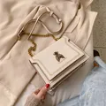 Chic cream crossbody bag featuring a gold bee emblem and textured leather finish - White