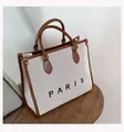 Detail of canvas tote bag with brown leather trim and PARIS print on wooden stool - Large / Brown