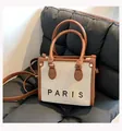 Detail of canvas tote bag showing Paris print, leather trim, and metal rivet accents - Small / Brown