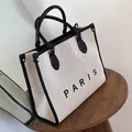 Large beige canvas tote bag with Paris print and black leather handles in a minimal setting - Large / Black