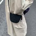 Detail einer schwarzen Halbmond-Umhängetasche aus Leder mit Quaste auf einem beigen Trenchcoat - Schwarz
