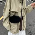 Minimalist black oval crossbody bag in matte suede texture shown in street style scene - Black