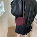 Chic burgundy oval crossbody bag in matte suede leather worn by a female model - Red