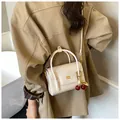 Detail of cream crossbody bag with gold metal logo and decorative red cherry pendant - With Cherry Pendant Style / White