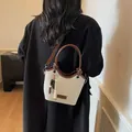 Beigefarbene Canvas-Eimertasche mit dunkelbraunem Leder am schwarzen Blazer - Weiß
